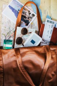 traveling bag with sunglass, a map, a phone, a ticket, and other papers